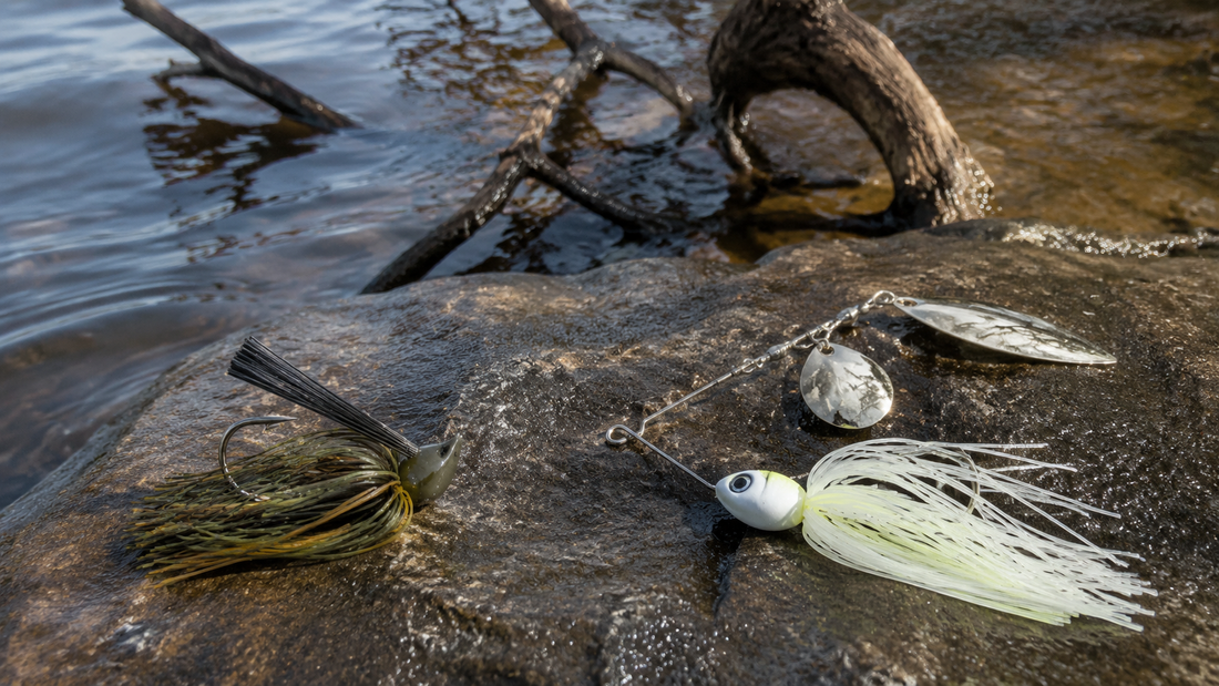 Bladed jig and spinnerbait placed on a wet rock beside stained freshwater with bass cover in the background
