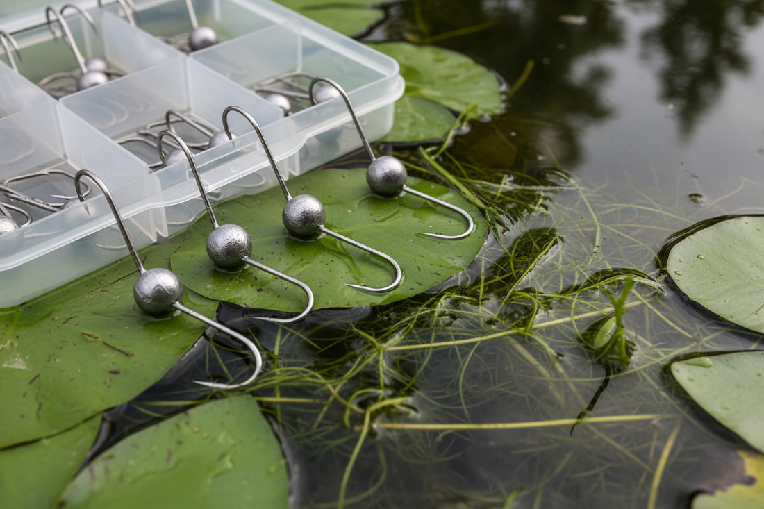 Weedless jig head hooks in multiple weights beside soft plastics and heavy bass cover