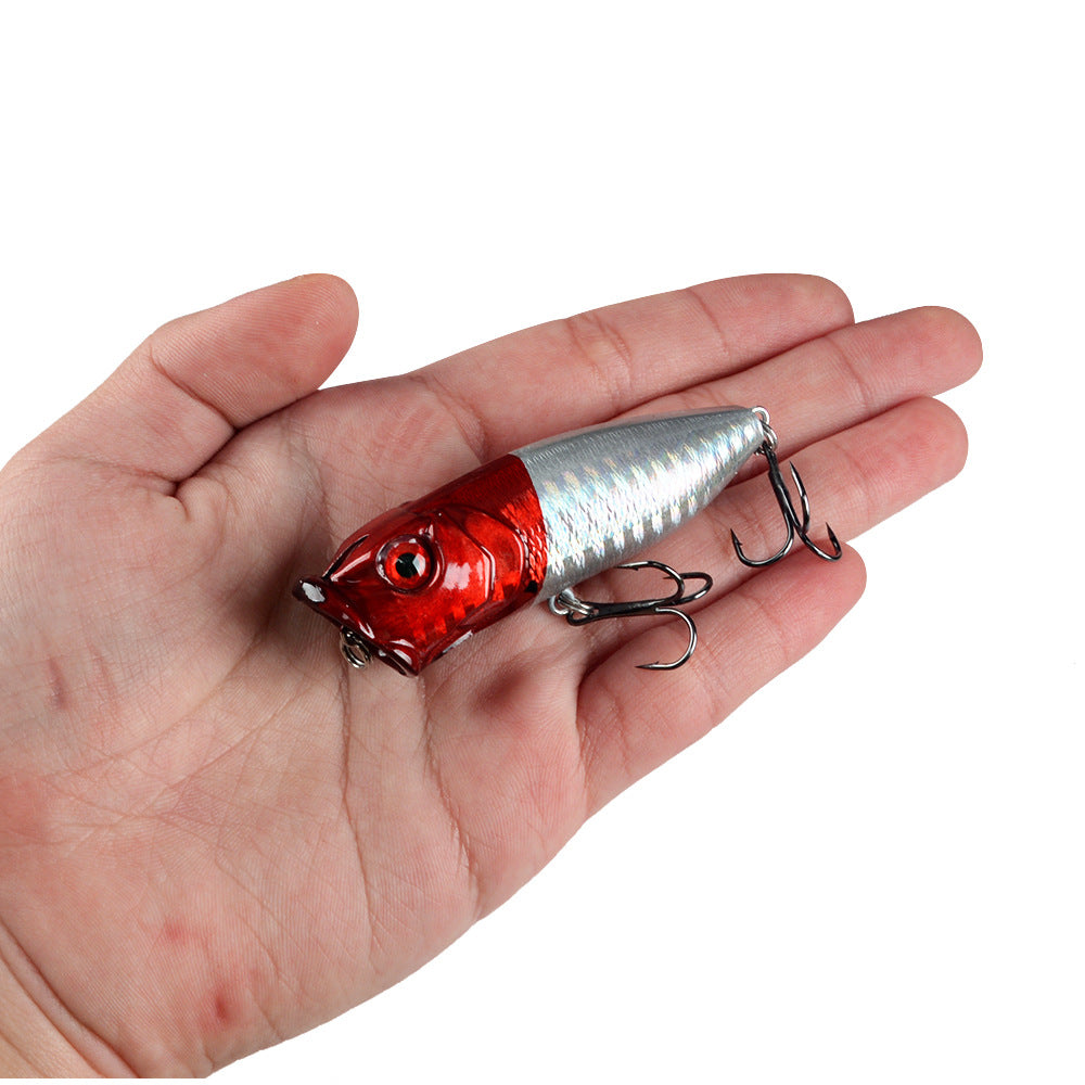 Small red and silver topwater popper lure with treble hooks held in palm